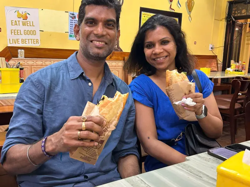 Two travelers holding bánh mì at a bánh mì shop in Hoi An
