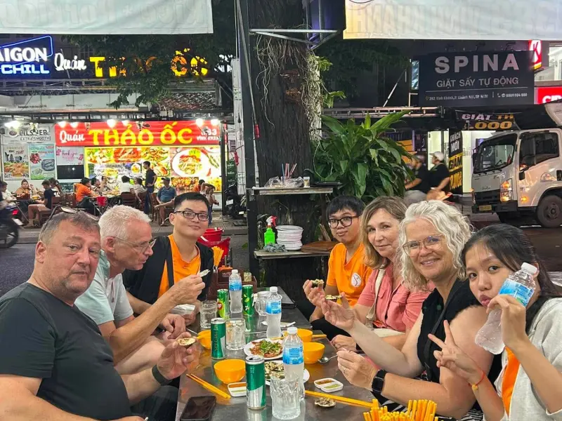 Guests sharing snails and drinks at a street food table in Saigon at night